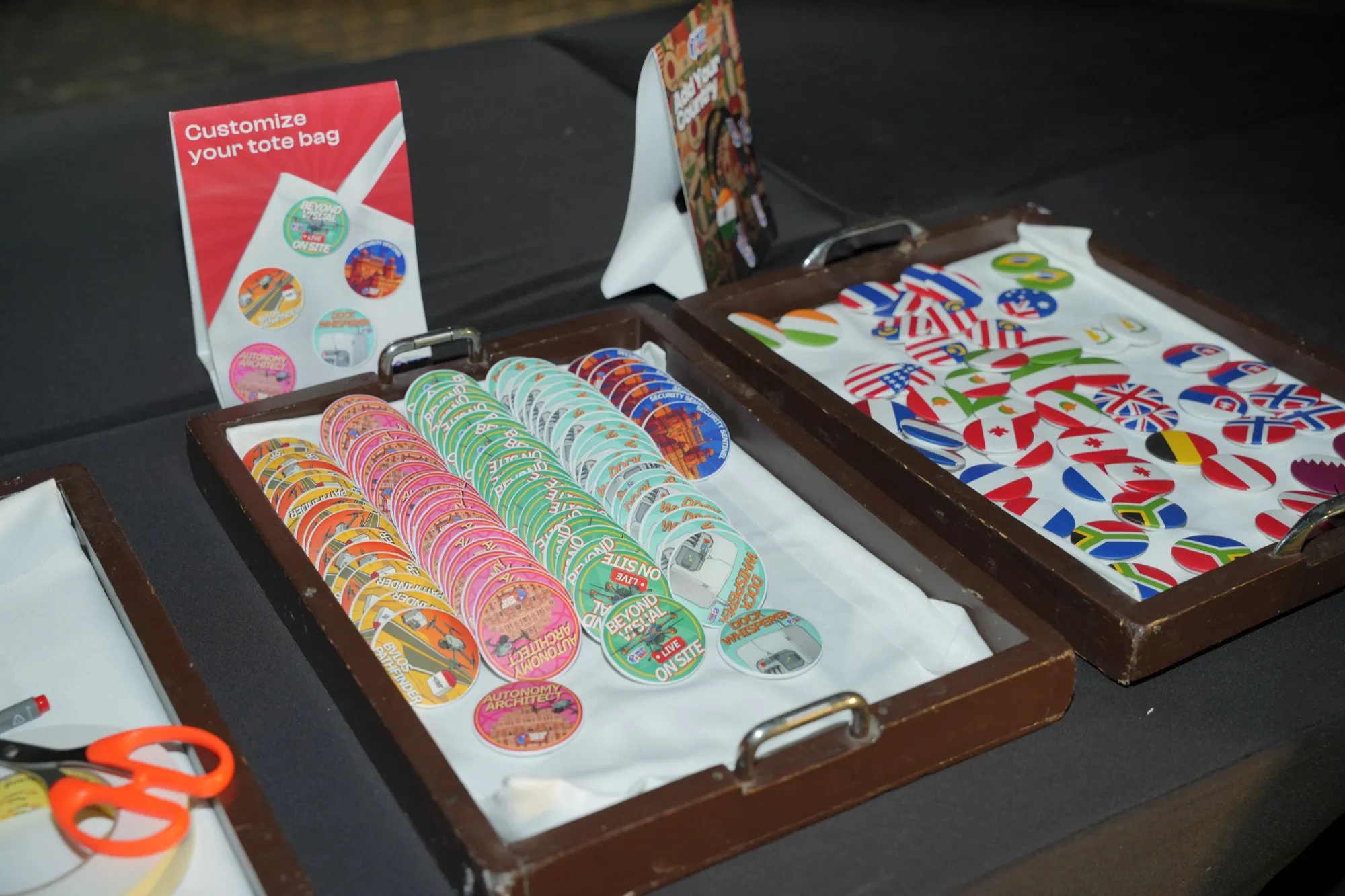 Trays of colourful pin badges and country flags beside a sign reading customise your tote bag