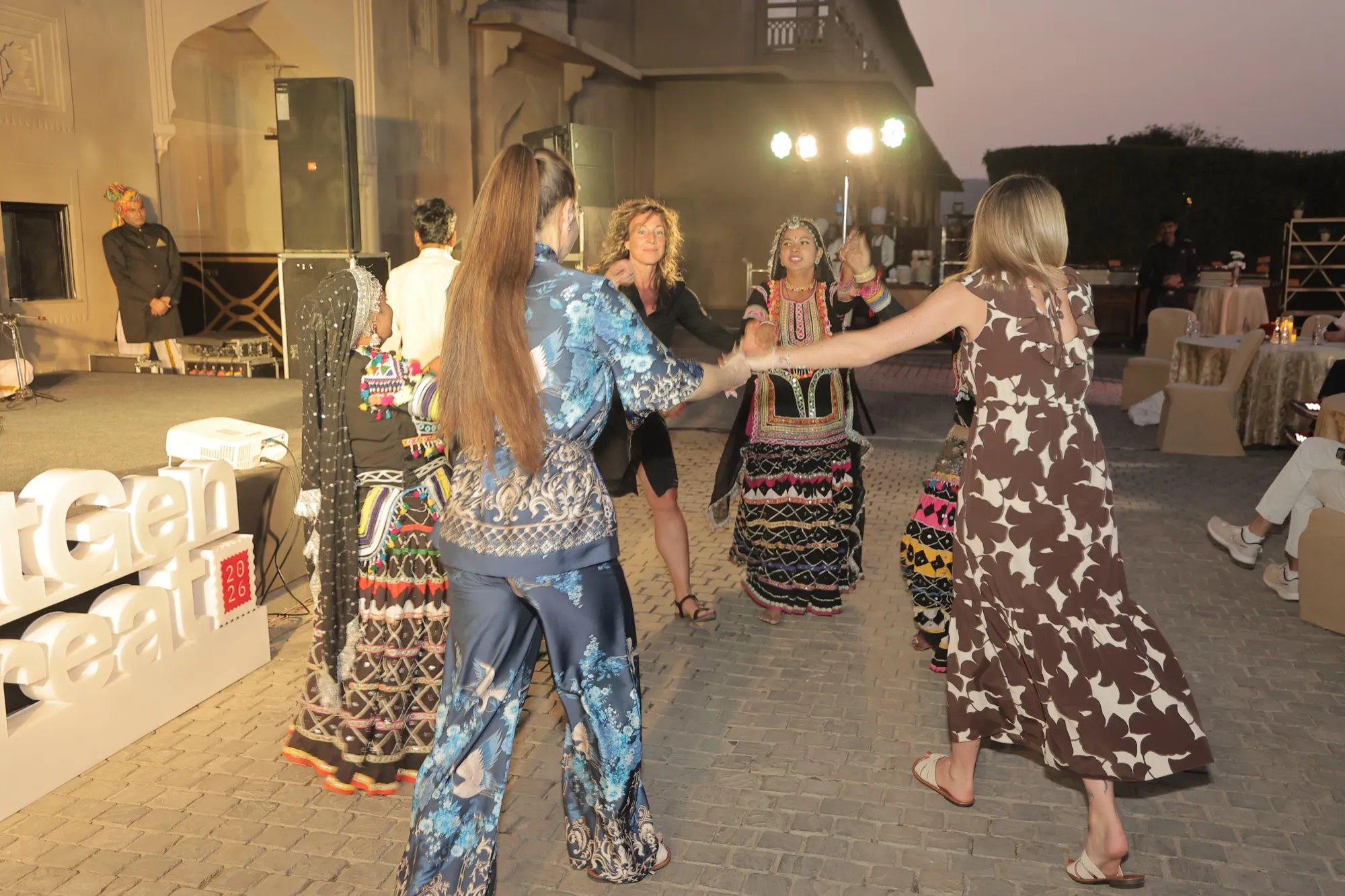 Guests and dancers holding hands in a circle on the courtyard
