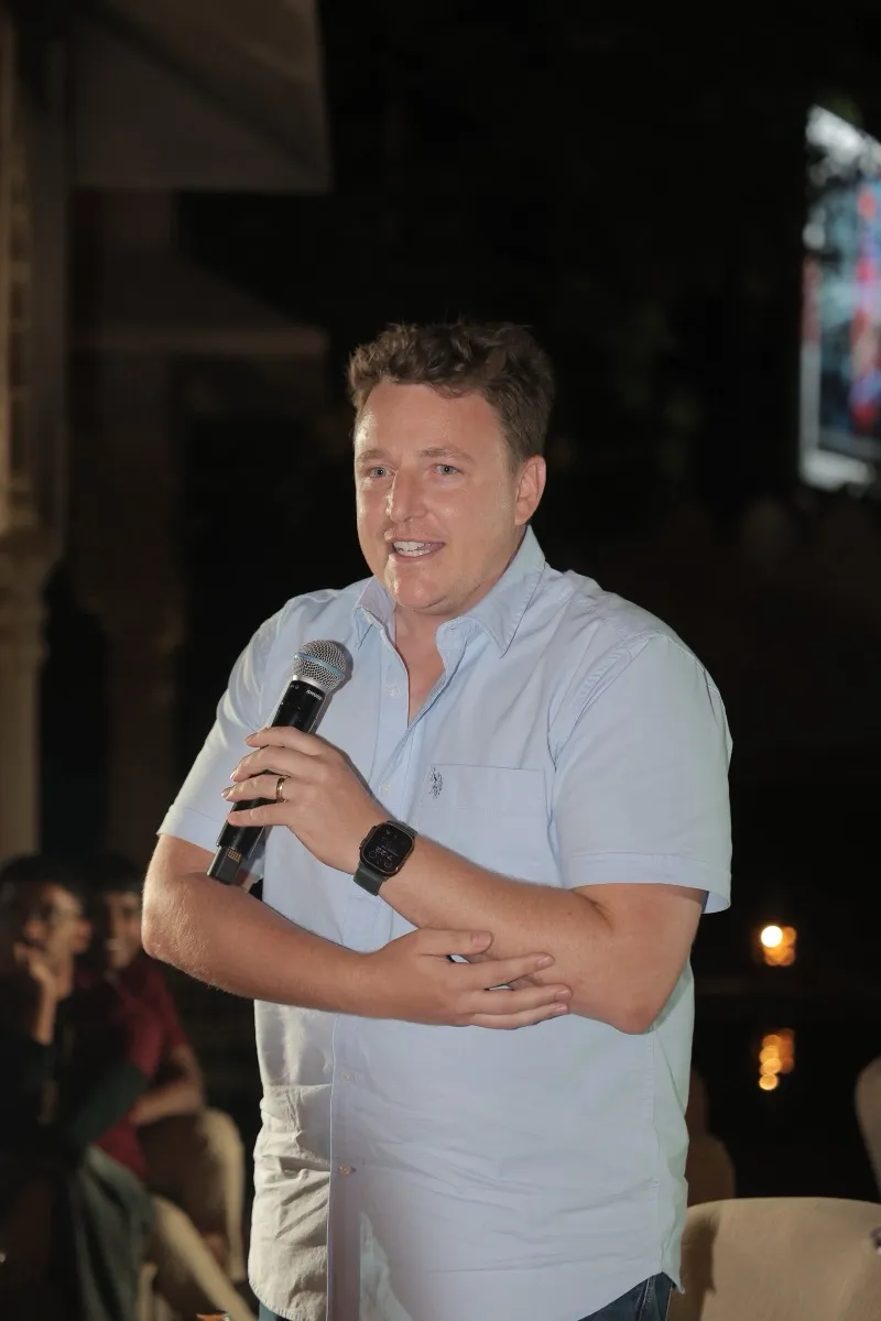 A guest with a microphone, smiling, on the courtyard stage at night