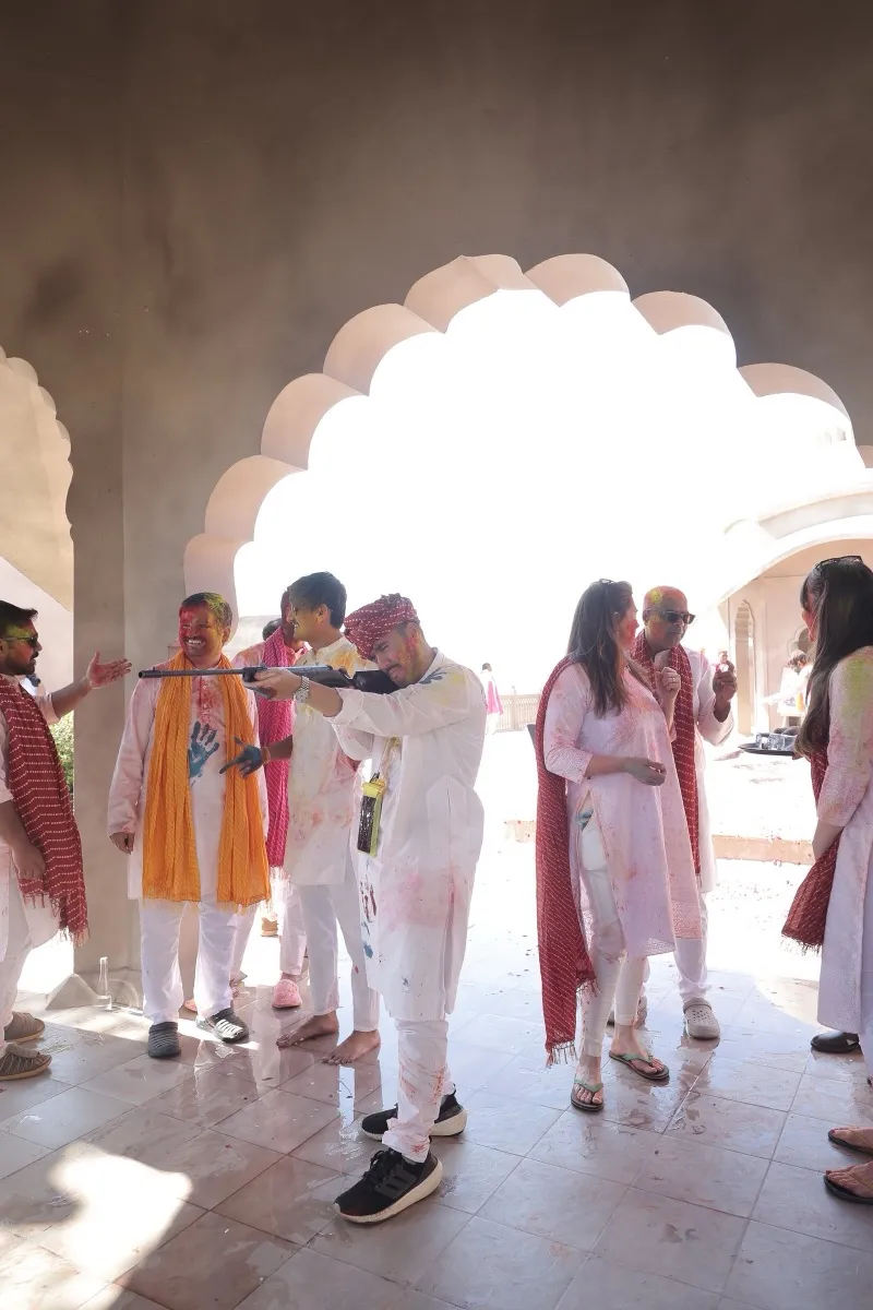 Guests in white and orange arriving through the arches for Holi