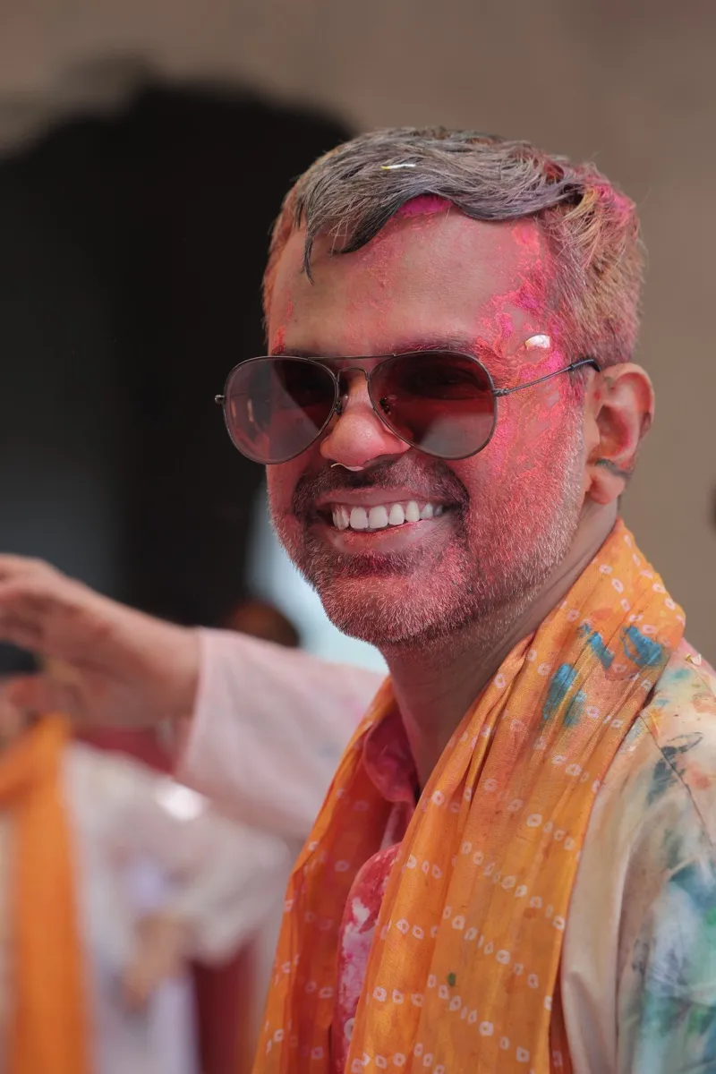 A guest in sunglasses grinning, his face dusted pink and blue