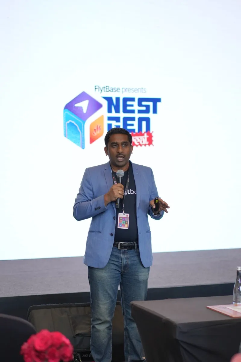 A FlytBase speaker on stage in front of the bright NestGen backdrop