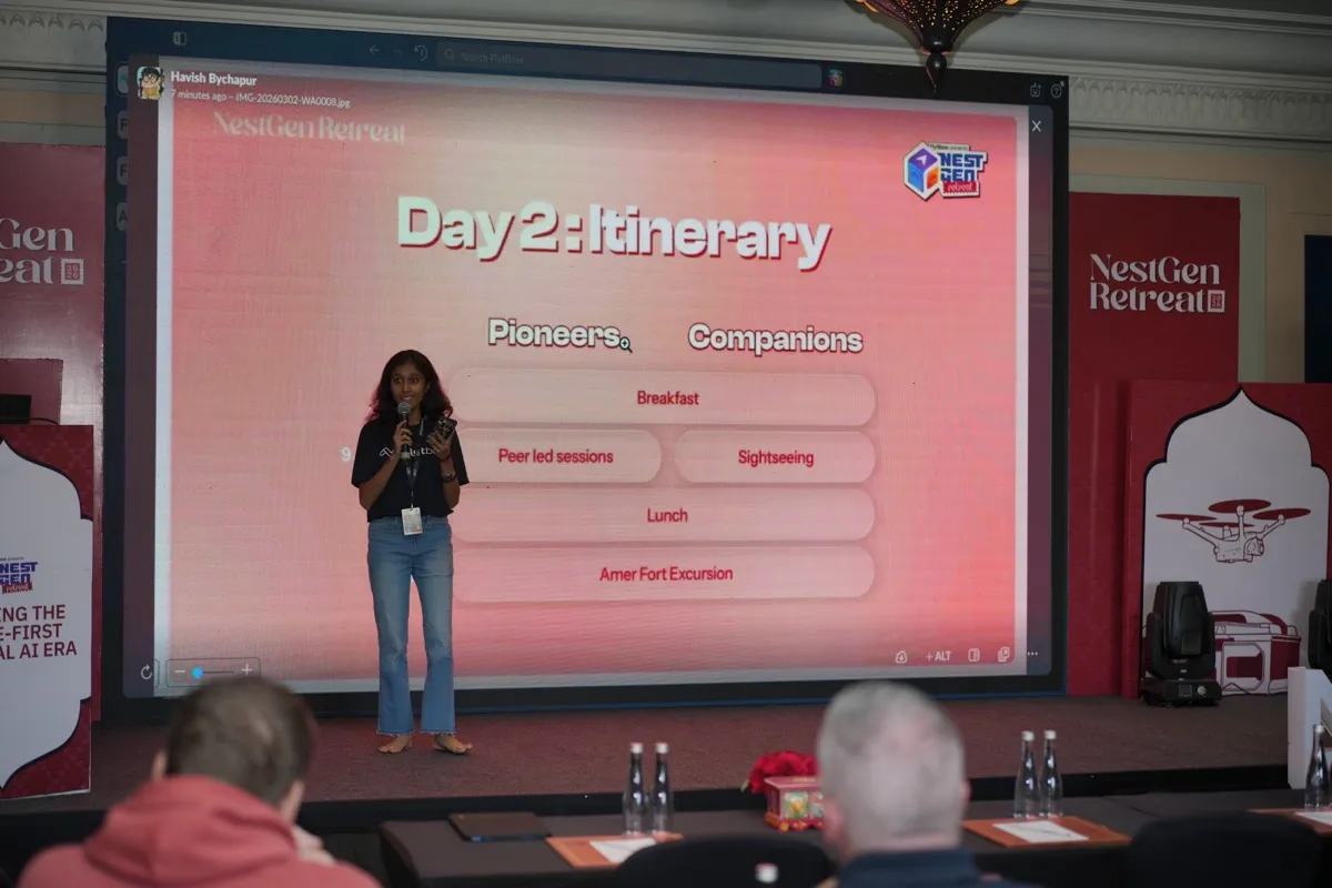 A host on stage presenting the Day 2 itinerary for pioneers and companions