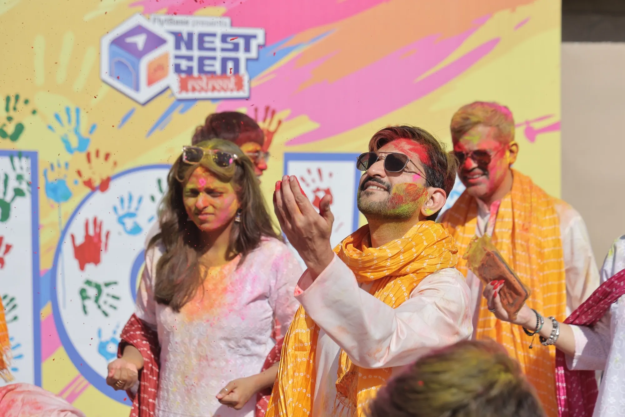 Guests throwing colour in front of the bright NestGen Holi backdrop