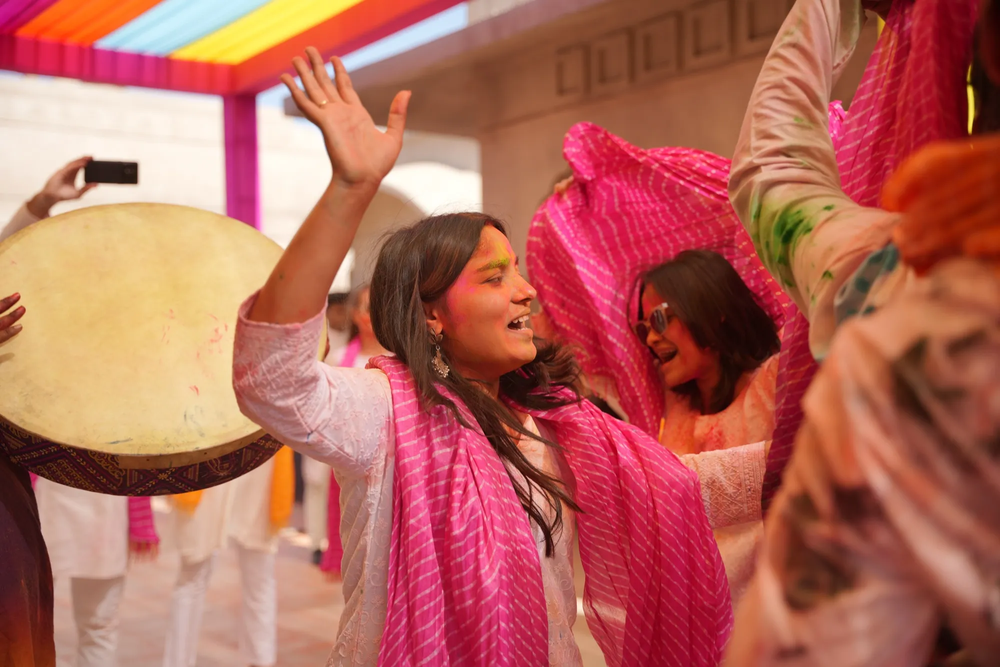 A dancer playing the daf among guests waving pink dupattas