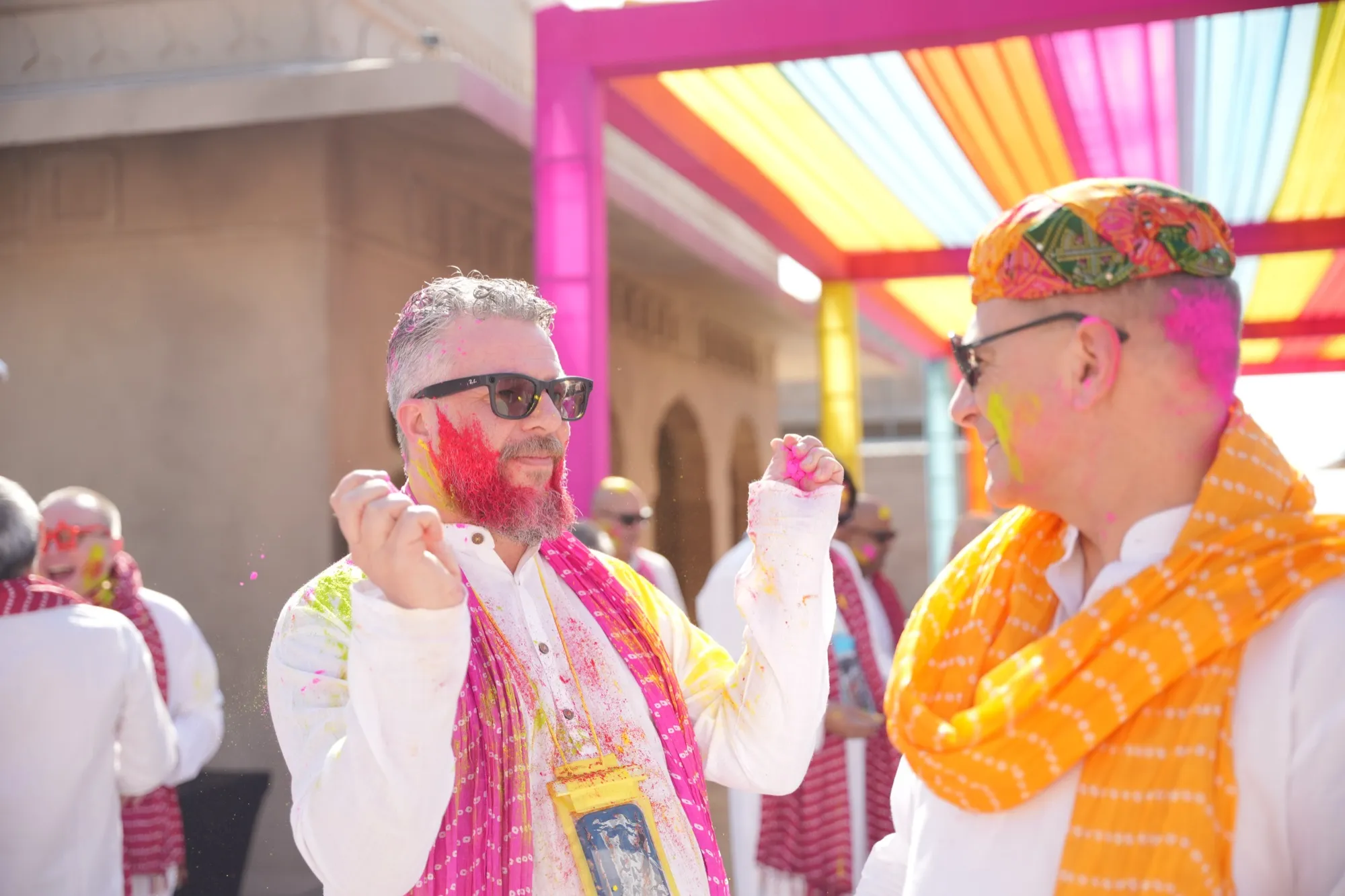 Two guests in sunglasses, faces streaked pink, under the coloured canopy