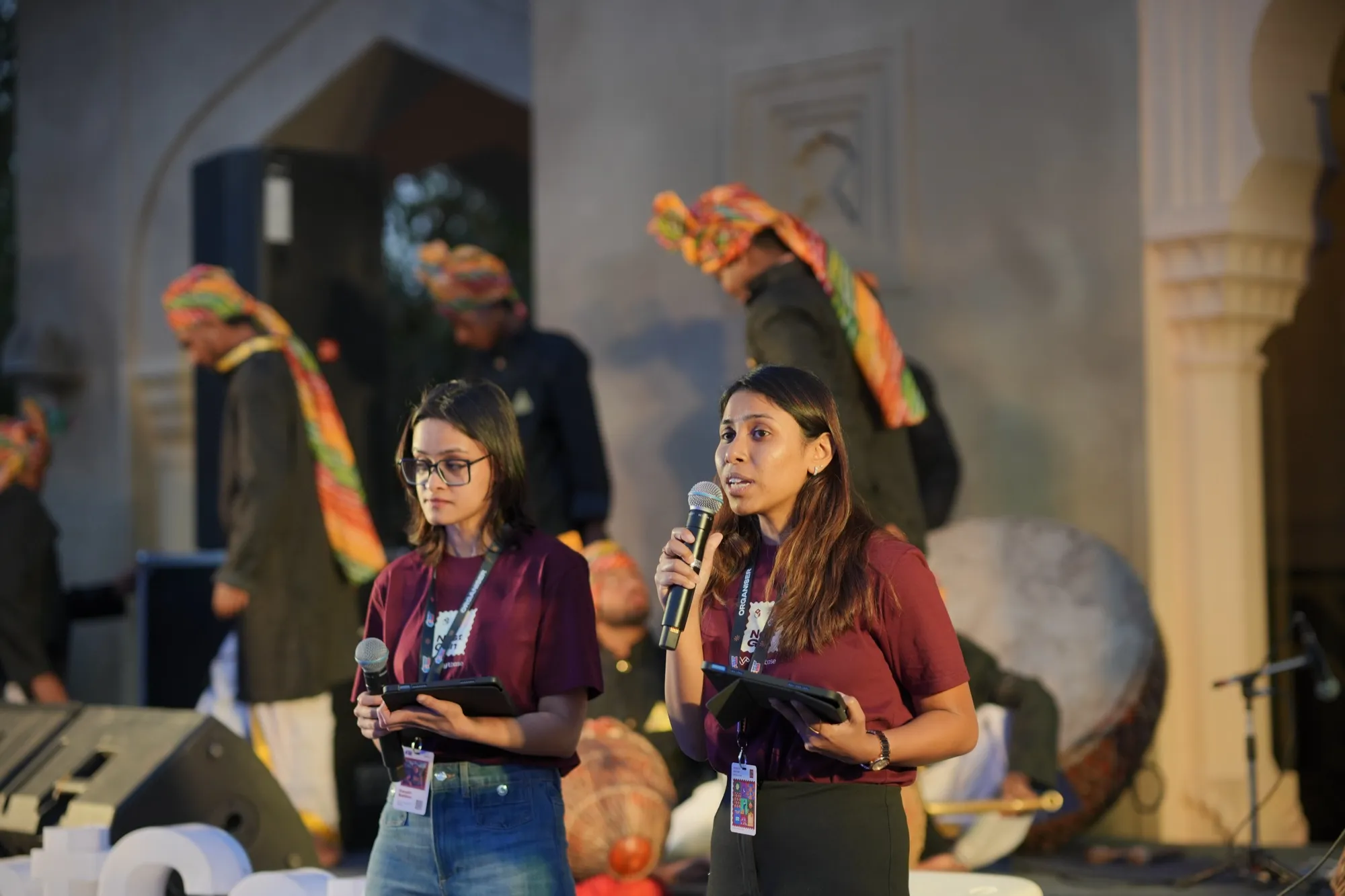 Two FlytBase hosts speaking on the stage at dusk