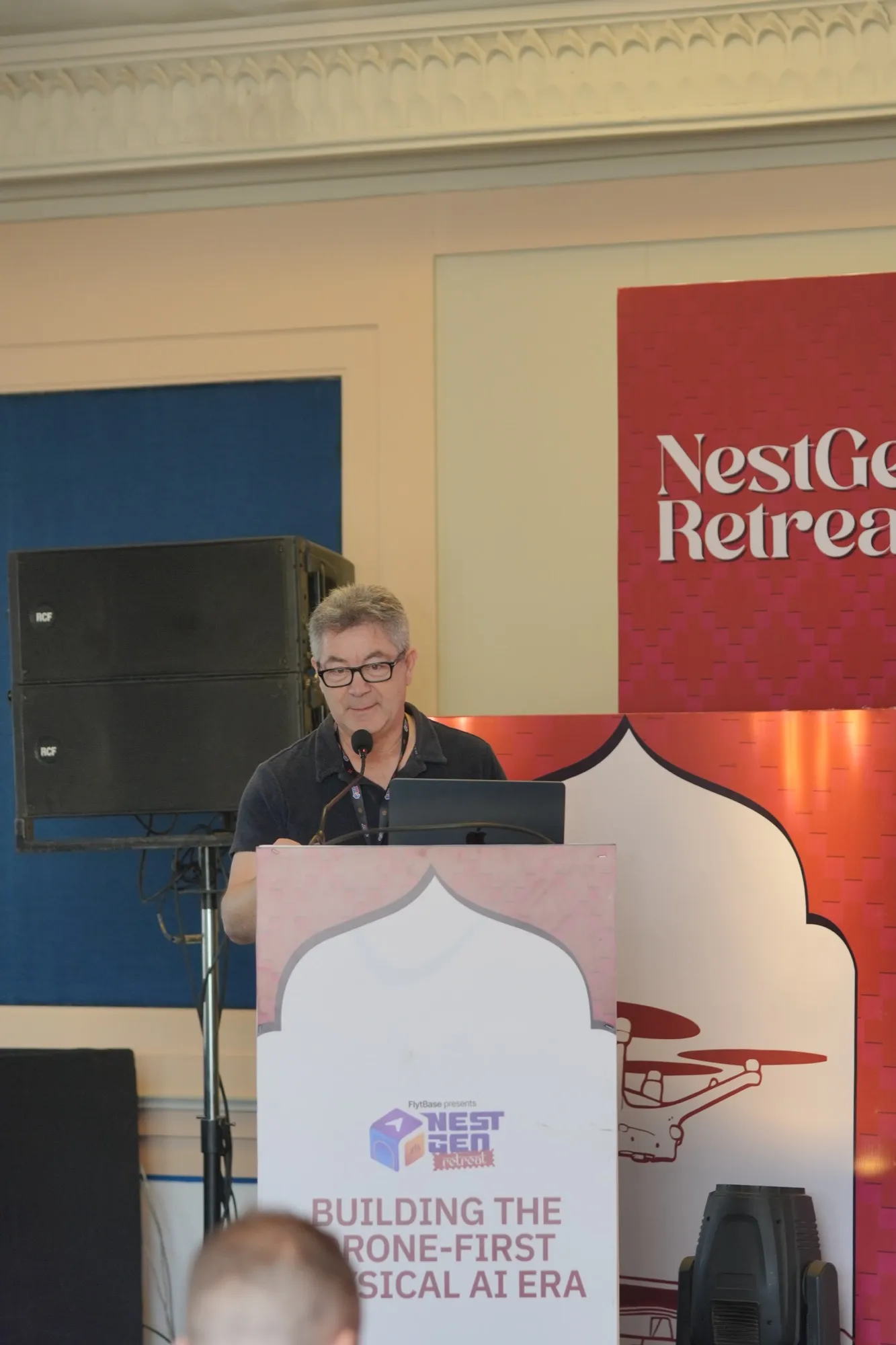 A pioneer speaking at the lectern beside the NestGen Retreat banner