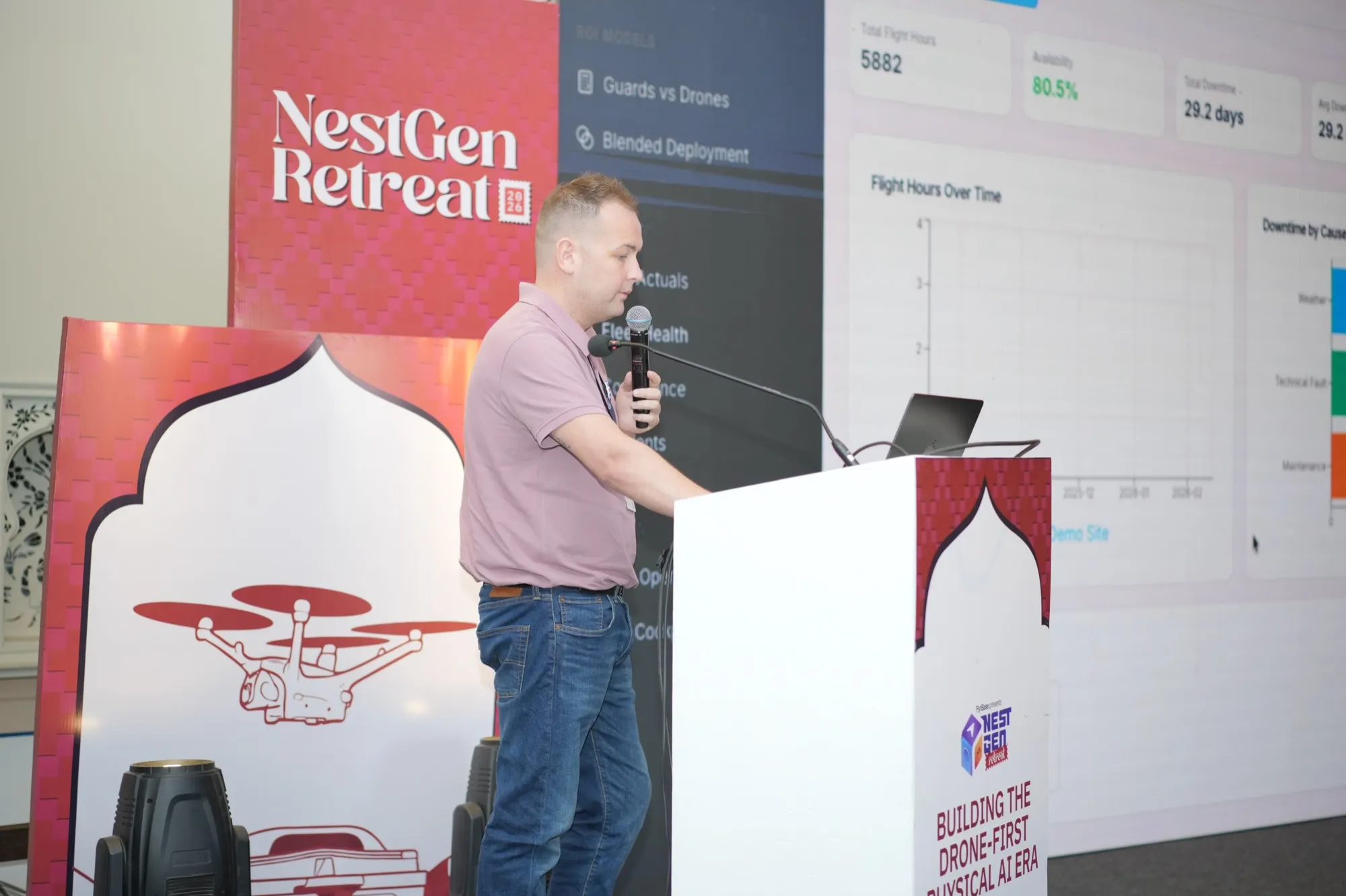A pioneer presenting from the lectern beside a dashboard on screen