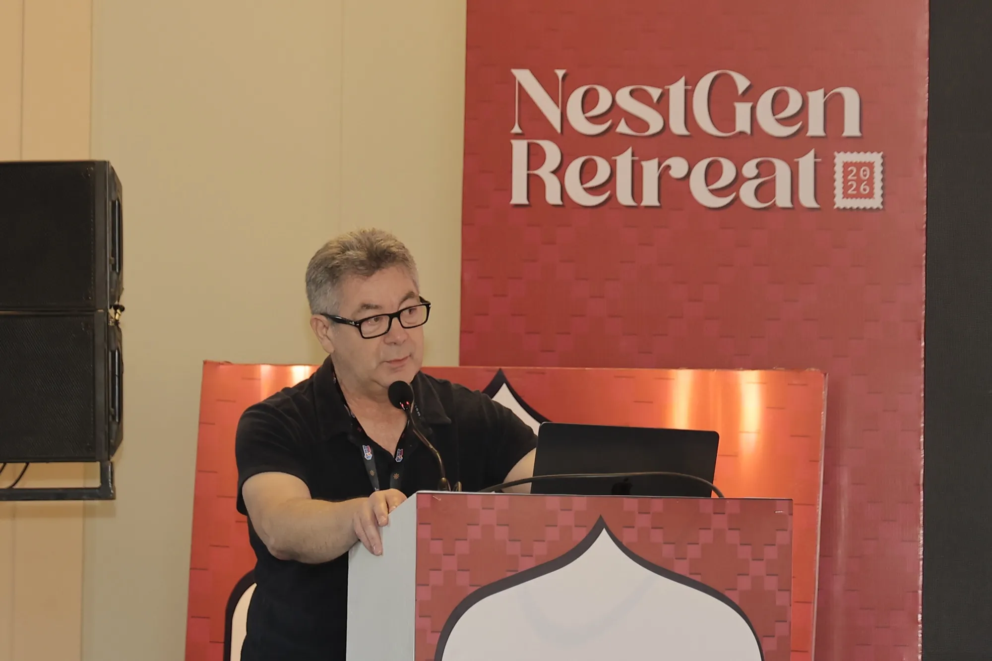 A pioneer at the lectern in front of the red NestGen Retreat wall