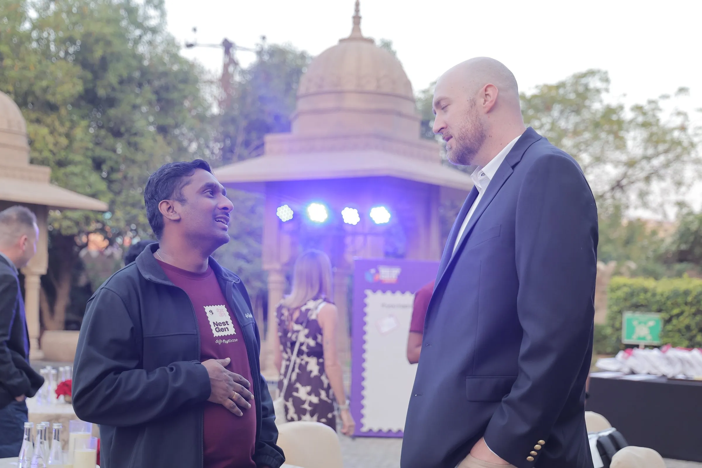 Two guests deep in conversation by a lit pavilion at the welcome evening