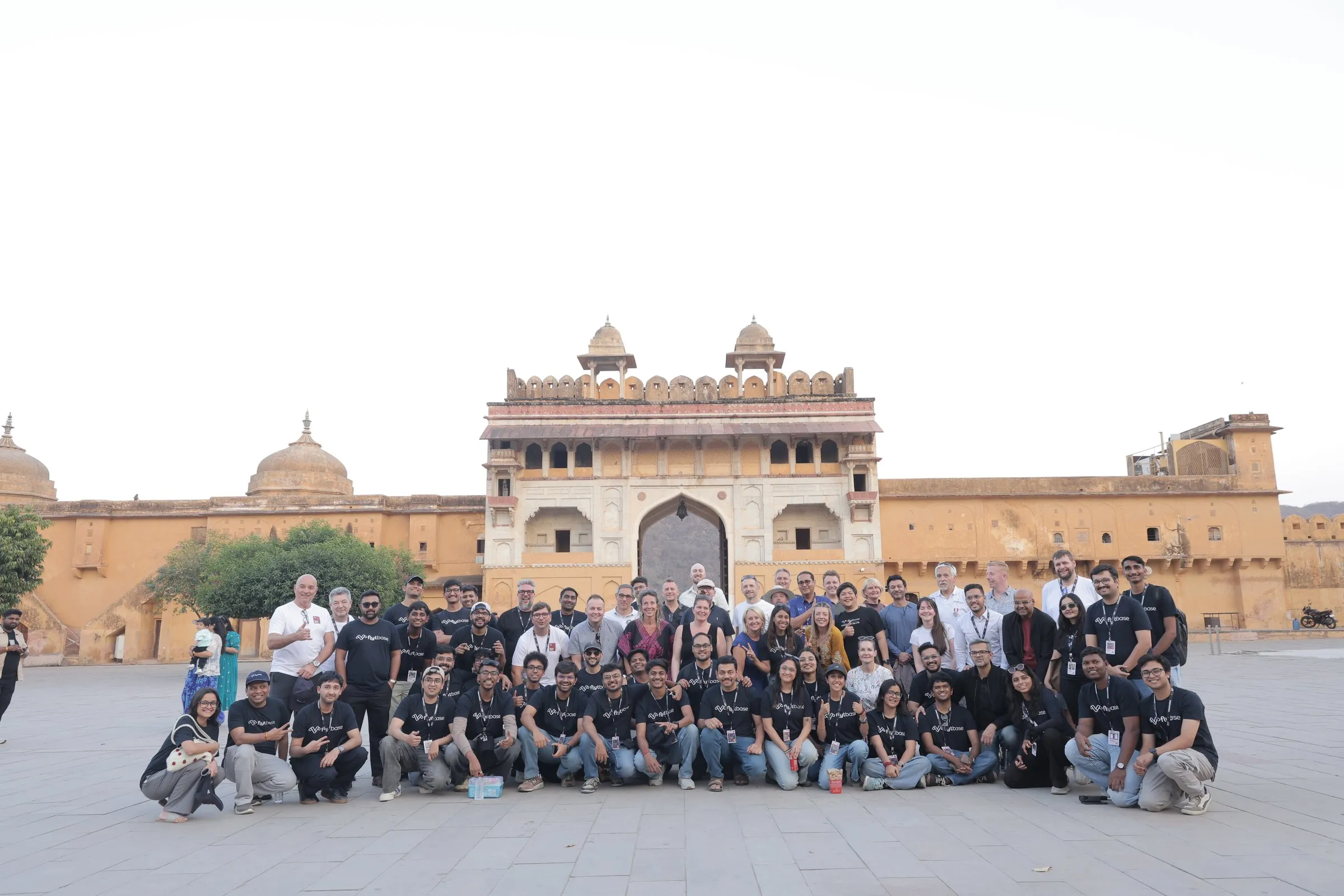 The whole group in black NestGen T-shirts in the courtyard of Amer Fort, the ochre gate behind them
