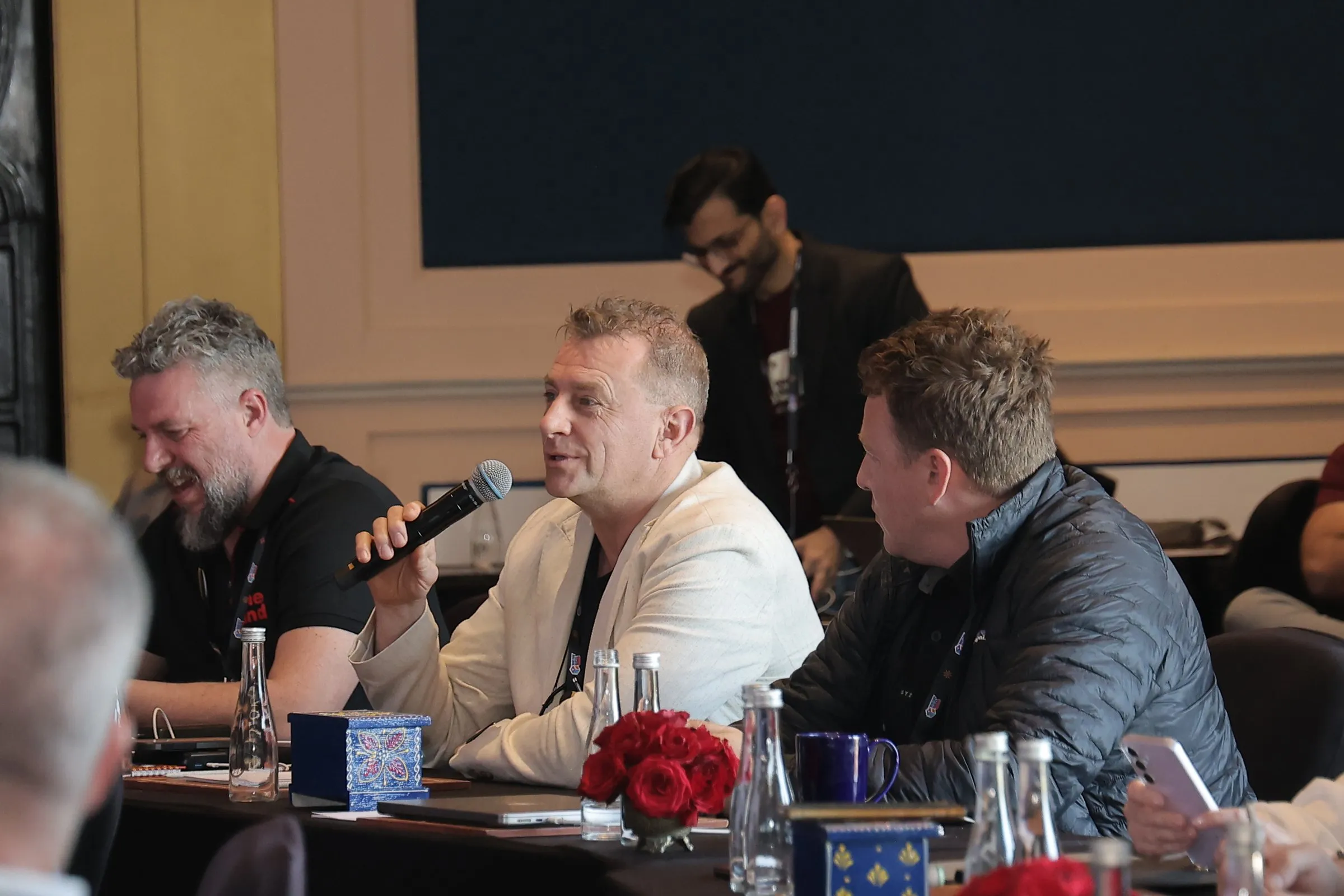 Three pioneers at a round table, one laughing into a microphone