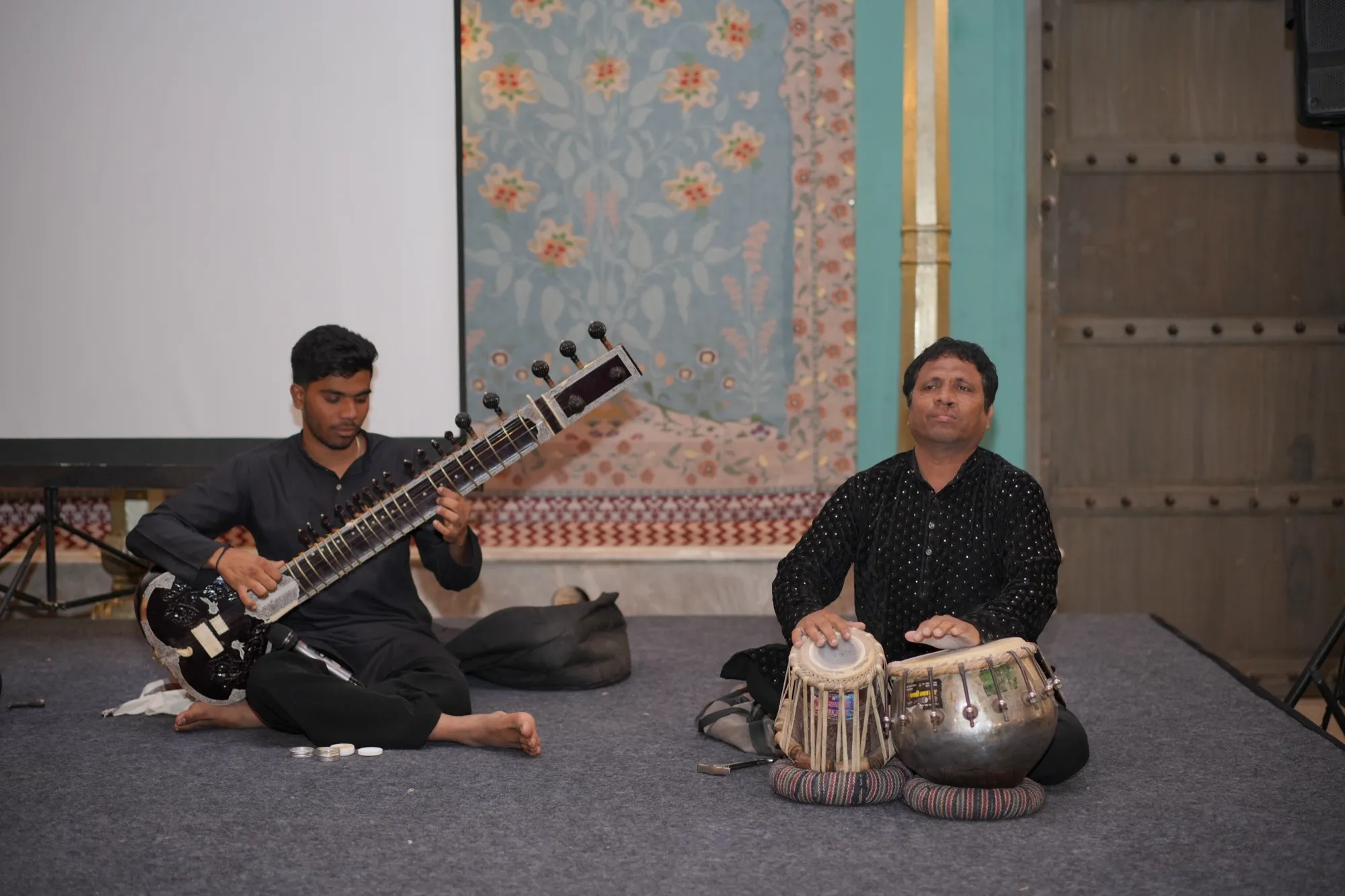 Two musicians on a low stage, one with a sitar, one with tabla